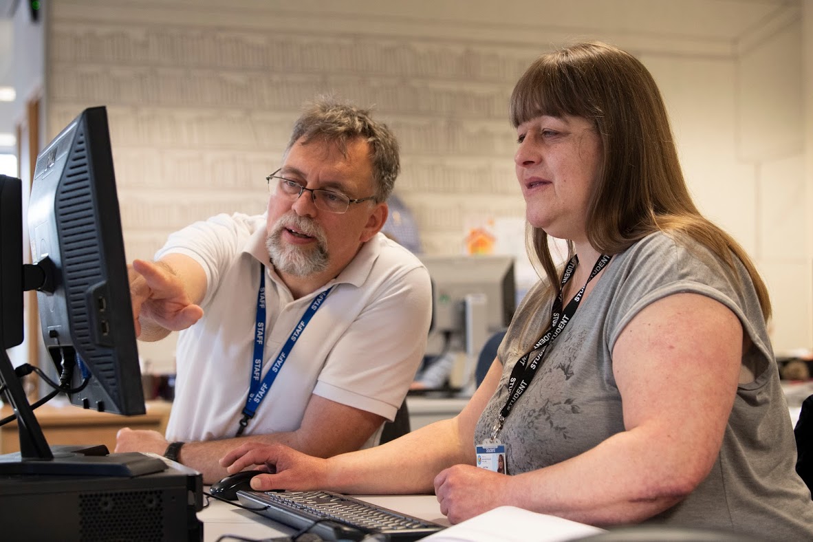 Teacher helping a student at a desk with a computer