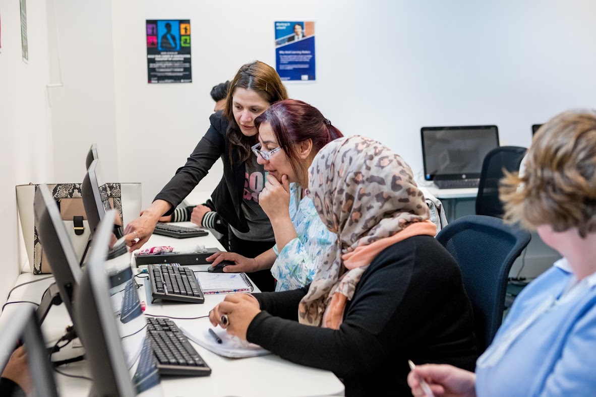 Students At Computers With One Being Helped By The Tutor